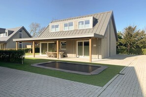 A modern house with a covered patio, a swimming pool, and a well-maintained lawn. - Villa in Kamperland with swimming pool (Kamperland)
