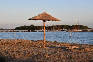 A beach with a thatched umbrella, a sandy shore, and a marina with boats in the background. - Villa in Kamperland with swimming pool (Kamperland)