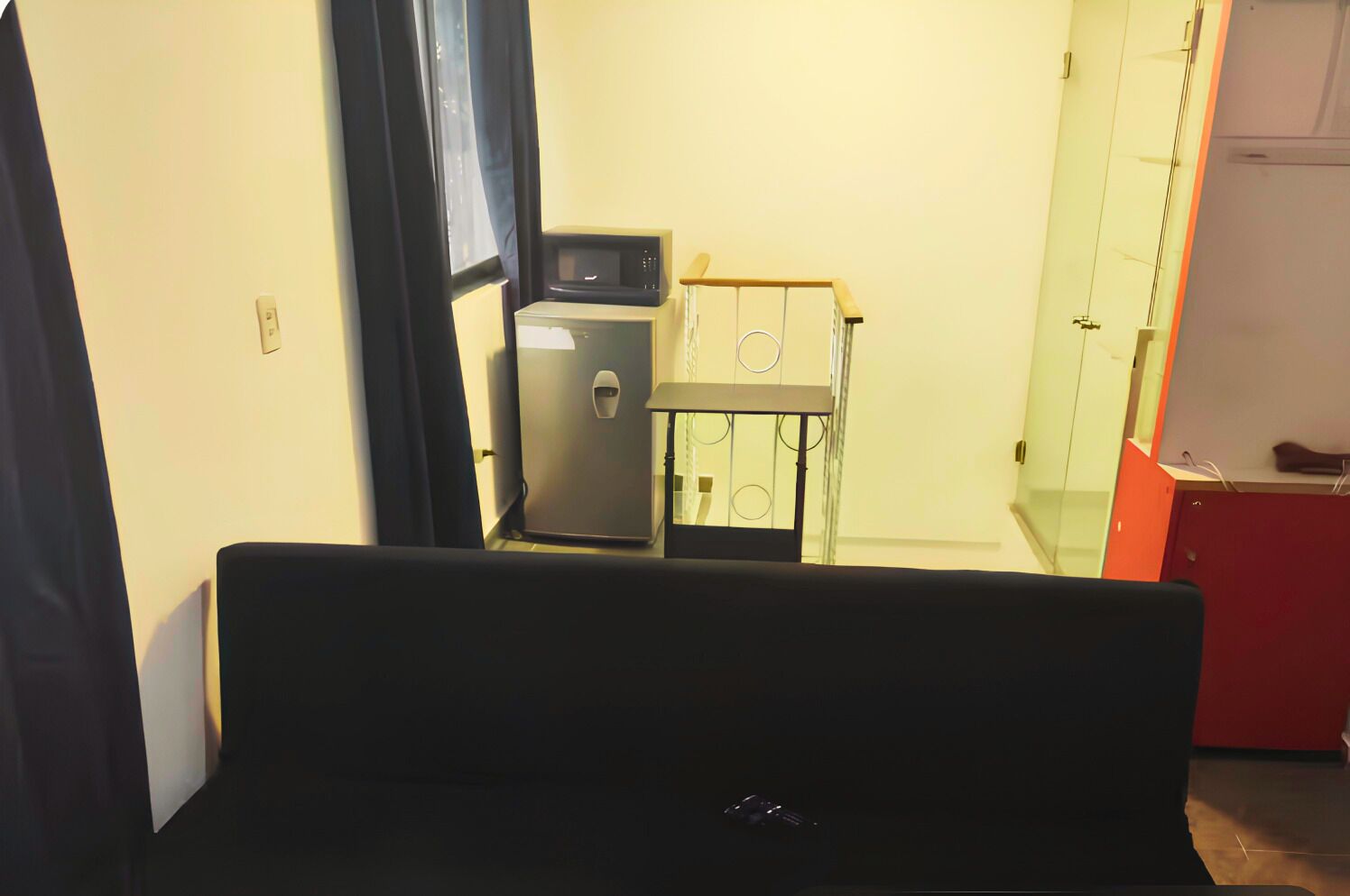 A room with a bed, a small kitchenette with a microwave and refrigerator, and a red cabinet.