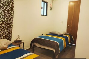 Une pièce avec deux lits, une petite table, une fenêtre et une porte.