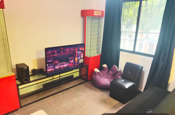 Un salon comprenant un téléviseur, un meuble rouge, un haut-parleur noir, un pouf violet et un canapé noir.