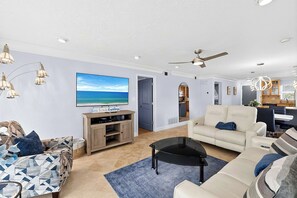 A modern living room with a flat-screen TV, a sofa, a coffee table, and a dining area with a kitchen in the background. - Siesta Key Condo Steps to Crescent Beach (Sarasota)