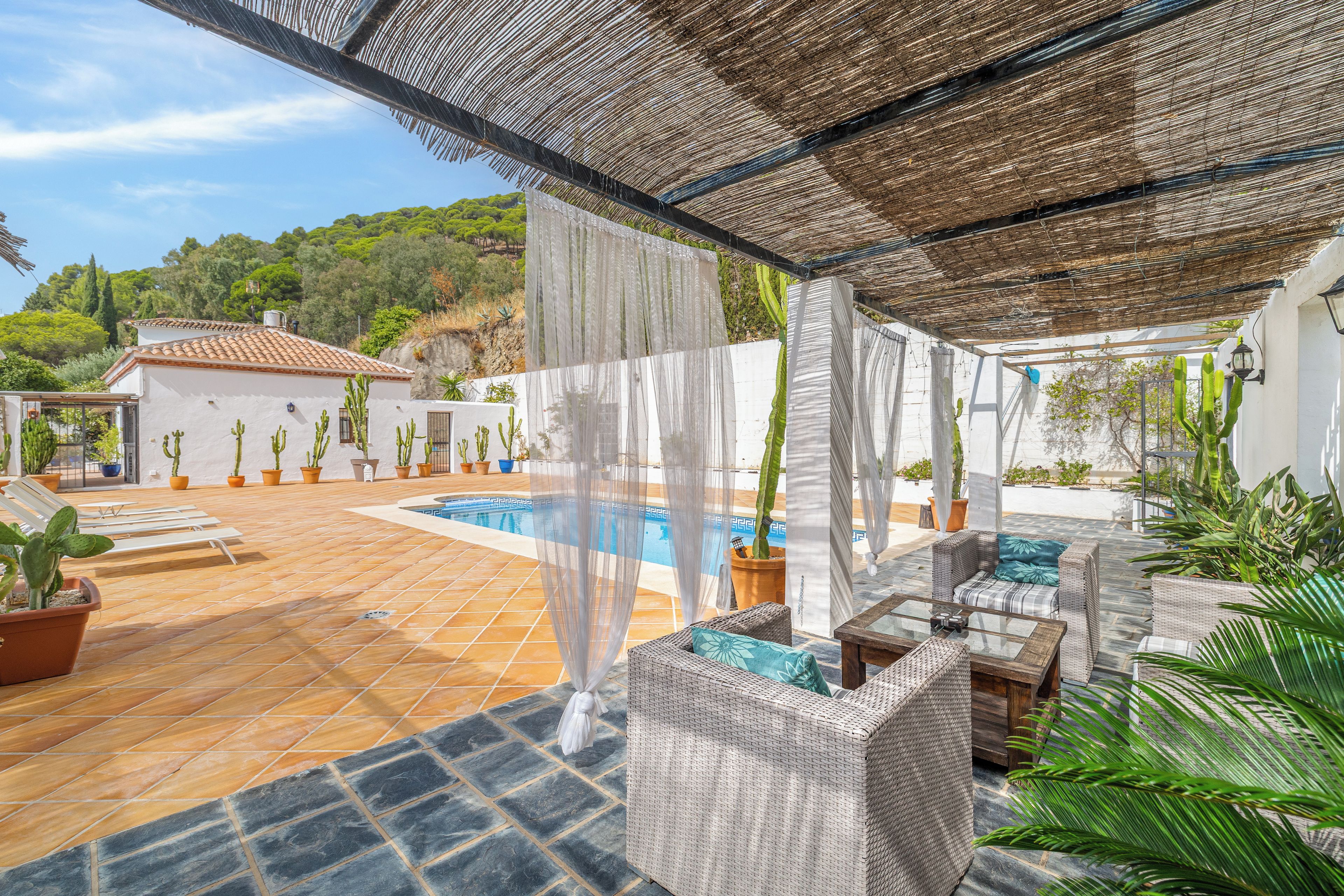 Un espacio al aire libre techado con piscina, sillas de descanso y plantas en macetas.