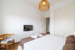 Una habitación de hotel con una cama, un televisor, una silla de madera y una puerta.