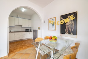 Una cocina moderna con armarios blancos, una zona de comedor con mesa y sillas de vidrio, y un cartel que dice 'WELCOME'.
