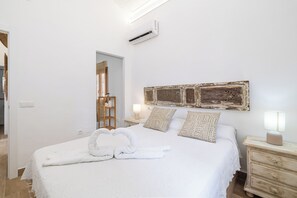 Ein ordentlich bezogenes Bett mit weißer Bettdecke und zwei Kissen mit Muster, einer Nachttischlampe und einer rustikalen Wanddekoration.