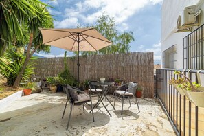 Un patio al aire libre con una mesa, sillas, una sombrilla grande y varias macetas con plantas.