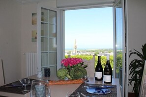 Une table à manger avec vue sur le paysage urbain, notamment sur le clocher d’une église, agrémentée de bouteilles de vin, de verres et d’une baguette.