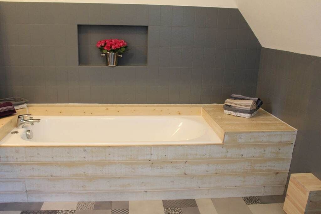 Ett modernt badrum med ett fristående badkar, en liten hylla med en vas med blommor och prydligt staplade handdukar.