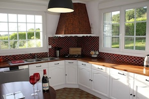 A kitchen with white cabinets, a wooden countertop, a black hanging light, and a window with a view of greenery.