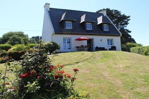 Une maison à deux étages, avec un toit en pente, une porte d’entrée et un petit porche surmonté d’un parasol rouge.