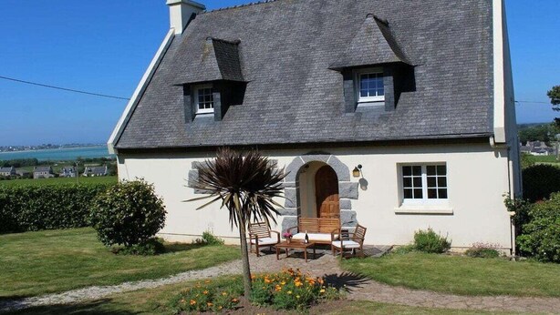 Ein Haus mit einem geneigten Dach, einem steinernen Bogen und einer kleinen Veranda mit Sitzgelegenheit.