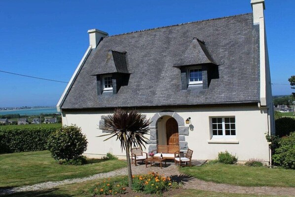 Une maison avec un toit en pente, une arche en pierre et un petit porche doté d’un espace pour s’asseoir.