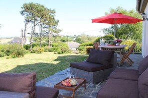 Une terrasse extérieure avec une table à manger, des chaises et un parasol rouge.