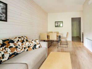 Ein Wohnzimmer mit einer Couch, einem Esstisch mit Stühlen, einem gerahmten Bild an der Wand und einem Flur, der in ein weiteres Zimmer führt.