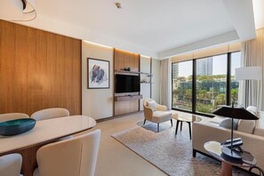 A modern living room with a dining area, a sofa, a TV, and a large window offering a city view. - Address Opera (Dubai)