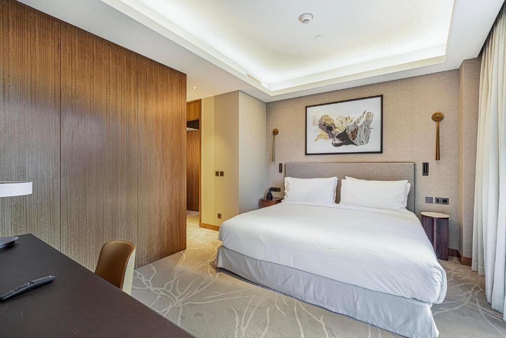 Ein Hotelzimmer mit einem großen Bett, einem Schreibtisch mit Stuhl, einem Nachttisch und einem Wandbild.
