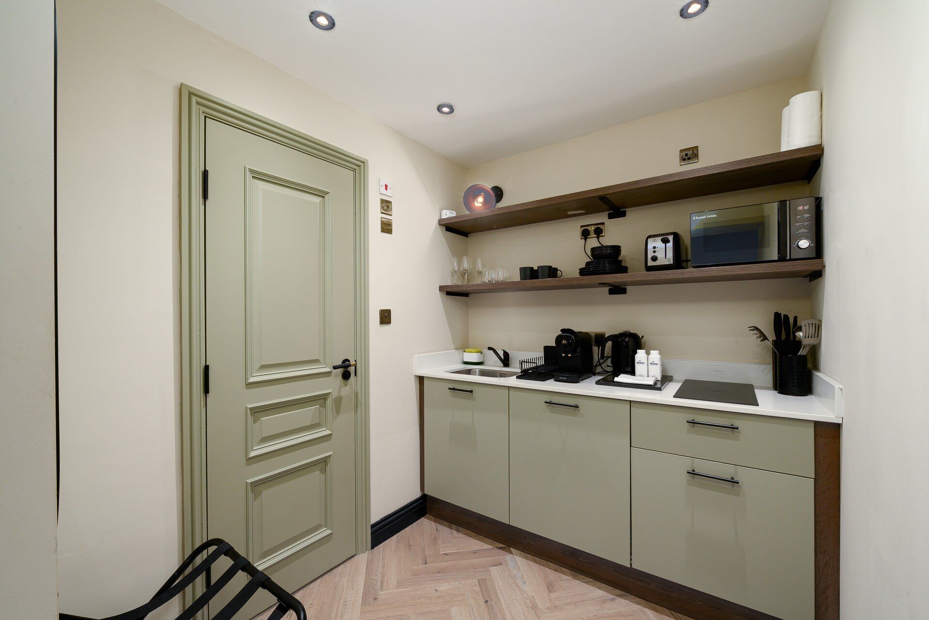 A compact kitchen with a microwave, coffee maker, and utensils on the counter.