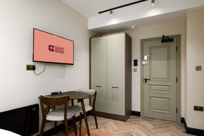 A hotel room with a dining table, chairs, a television displaying 'GUEST READY', a wardrobe, a door with a lock, and a light fixture on the ceiling. - GuestReady - Stylish studio in Euston (London)