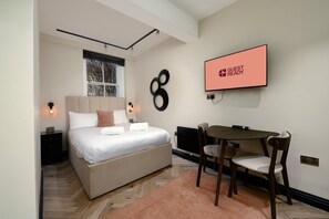 A bedroom with a bed, bedside tables, a TV, and a desk with chairs. - GuestReady - Stylish studio in Euston (London)