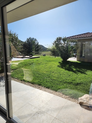 A view through a glass door of a well-maintained lawn with a stone wall and a building with a tiled roof. - Le Grand Rouvière Private Estate - Luxury Villa (Roquefort-la-Bédoule)