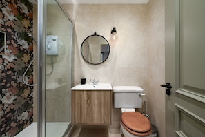 Ein Badezimmer mit Duschkabine aus Glas, Toilette, Waschbecken mit Holzausstattung und rundem Spiegel mit Beleuchtung.