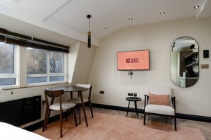 A modern room with a dining area, a television, a mirror, and a window with a view of trees. - GuestReady - Delightful retreat in Euston (London)