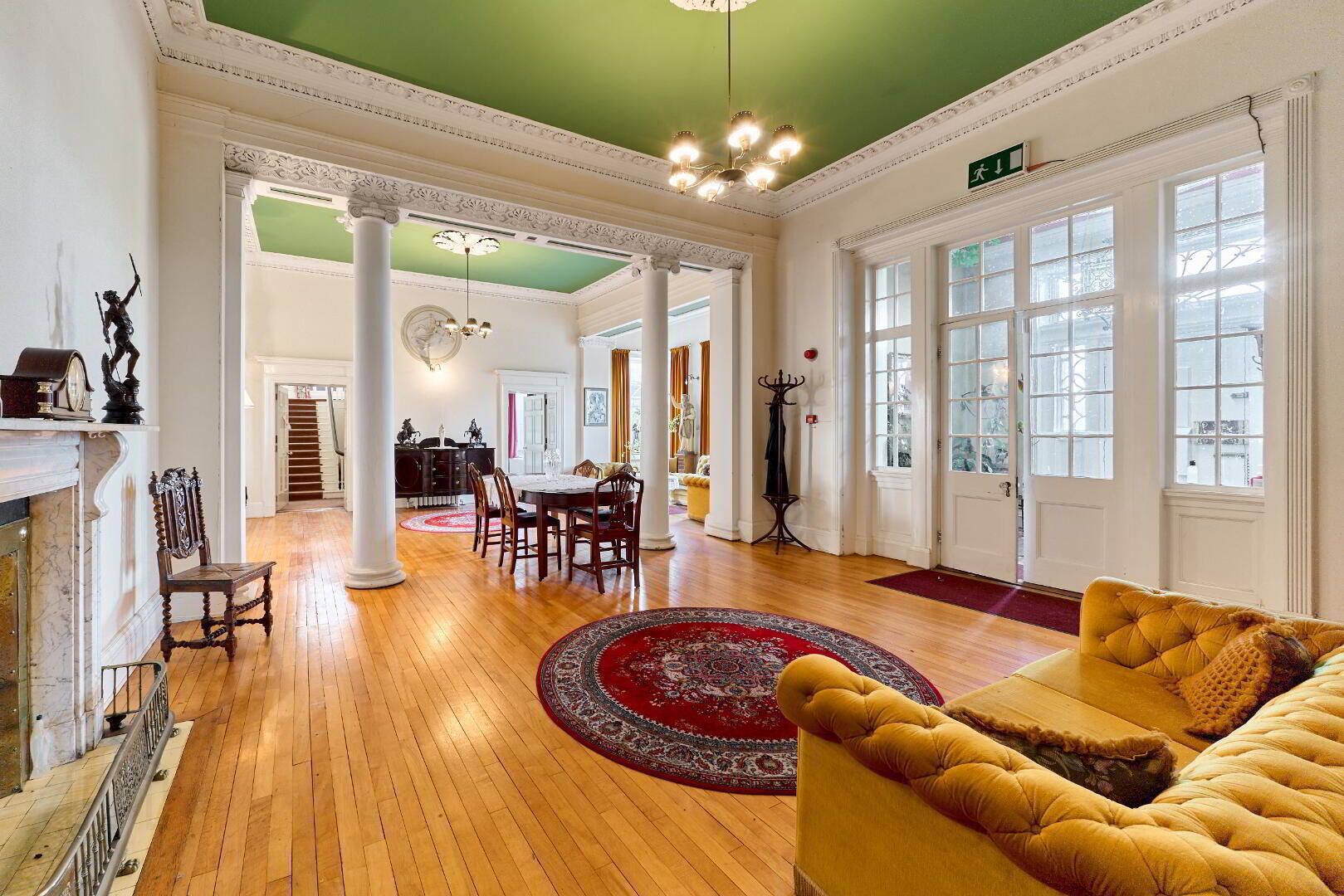 A spacious room with a wooden floor, a round red rug, a yellow sofa, and a fireplace.