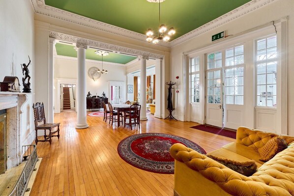 A spacious room with a wooden floor, a round red rug, a yellow sofa, and a fireplace.