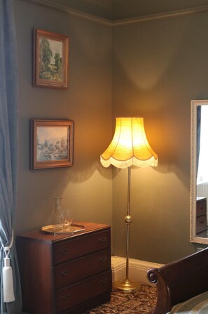 Una habitación con un aparador de madera, una lámpara de pie y dos cuadros en la pared.