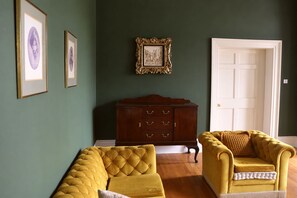 A room with a dark green wall, a wooden cabinet, two yellow armchairs, and a white door.