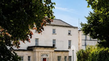 A building with a symmetrical facade, a central entrance with a red door, and a basketball hoop in the foreground.