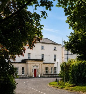 A building with a symmetrical facade, a central entrance with a red door, and a basketball hoop in the foreground. - South Hill House, Historic Georgian manor with capacity for 52 guests (Delvin)