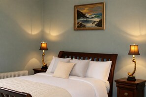 A bedroom with a bed, two bedside lamps, a painting on the wall, and a radiator.