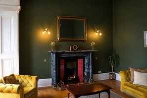 Una habitación con chimenea, dos sillones, una mesa y un espejo en la pared.