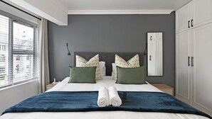 Un dormitorio moderno con una cama grande, dos almohadas, una colcha azul y una cama bien hecha.