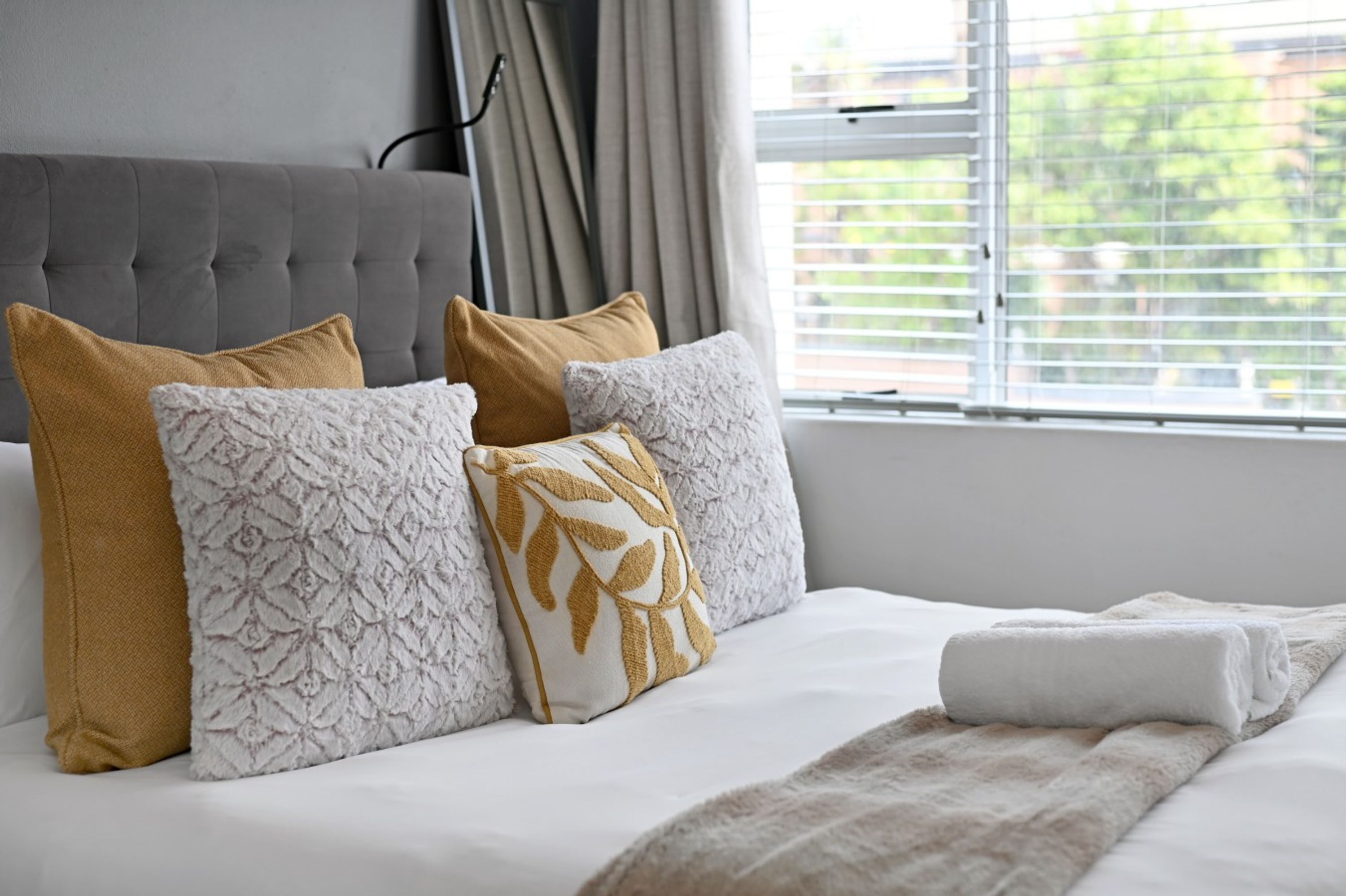 A neatly made bed with a white duvet and several pillows, including a patterned one.
