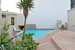 A swimming pool with a brick border, surrounded by potted plants and a palm tree. - Sea Point 2bed Home Spacious Central Secure (Cape Town)