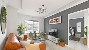 Una sala moderna con un sofá de cuero, un comedor, un televisor de pantalla plana y un ventanal grande.