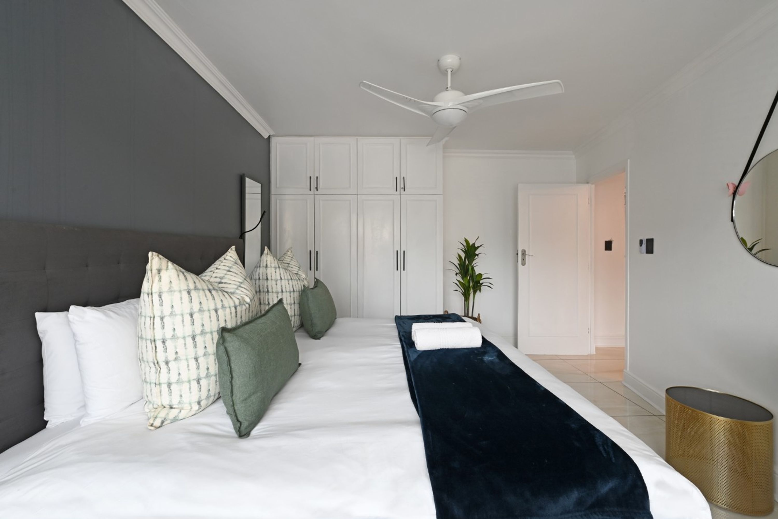 Quarto moderno com cama, travesseiros, mesa de cabeceira, ventilador de teto e guarda-roupa.