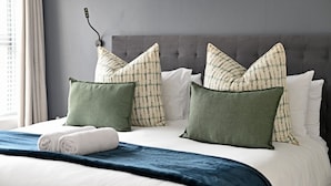 Una cama bien hecha con un edredón azul, almohadas blancas y almohadones verdes.