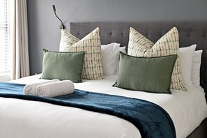 A neatly made bed with a blue blanket, white pillows, and green accent pillows. - Sunlit 2 Bedroom in the Heart of Sea Point (Cape Town)