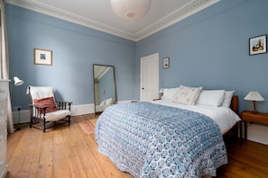 A bedroom with a large bed, a chair, a dresser, a mirror, and a door. - GuestReady - Stylish Victorian Home with Garden (London)