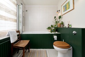 Et badeværelse med badekar, toilet, en træstol og en potteplante.