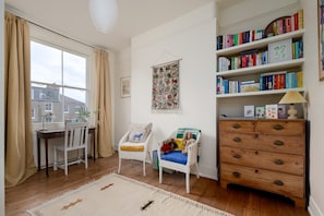 A cozy room with a large window, a bookshelf, a desk, and a chair. - GuestReady - Stylish Victorian Home with Garden (London)