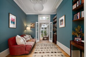 A hallway with a red sofa, a patterned rug, and a bookshelf with books. - GuestReady - Stylish Victorian Home with Garden (London)