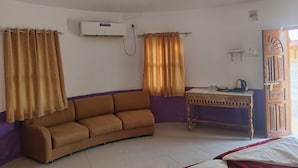 A room with a sofa, a table with a kettle, and an air conditioning unit on the wall.