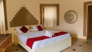 Una habitación de hotel con una cama, una mesita de madera, un adorno en la pared y una ventana con cortinas.