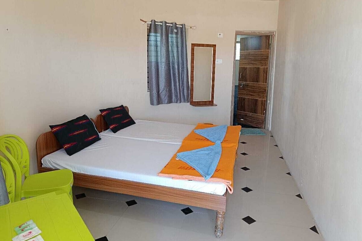 A single-bed room with a wooden headboard, a small bedside table, a mirror, and a window with curtains.