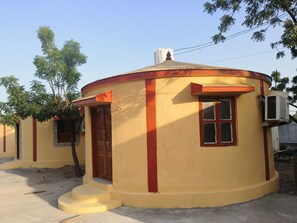 A circular building with a red door and window, surrounded by trees.